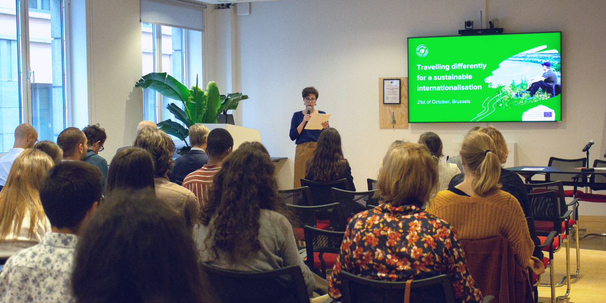 A photo of a person speaking in front of an audience.