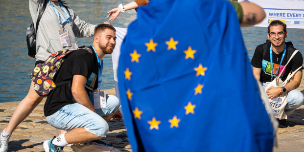 A picture of young people and an EU flag in front of them.