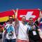 A group of young people holding a big flag made of many other country flags.