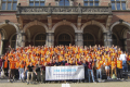 A big group of people in orange shirts posing for a picture and holding a flag of ESN Groningen.