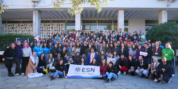 A big group of people posing for a picture with a flag of ESN Greece.